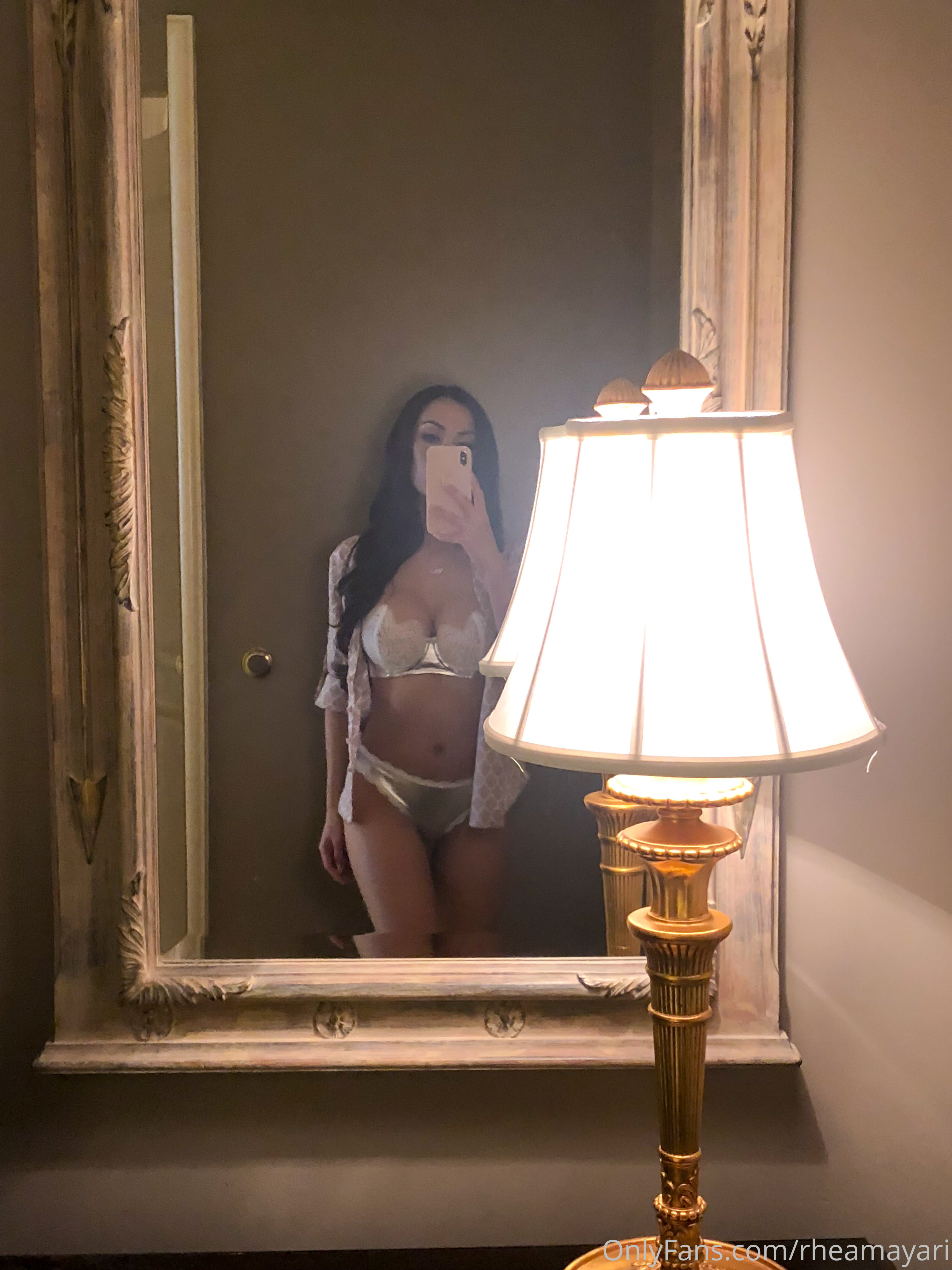 Vanessa Rallonza, a petite Filipino-American woman with dark brown hair, strikes a seductive pose in front of a mirror, showcasing her curvaceous figure in lingerie. Her nude skin glistens in the light, teasing the viewer with a hint of what's to come.