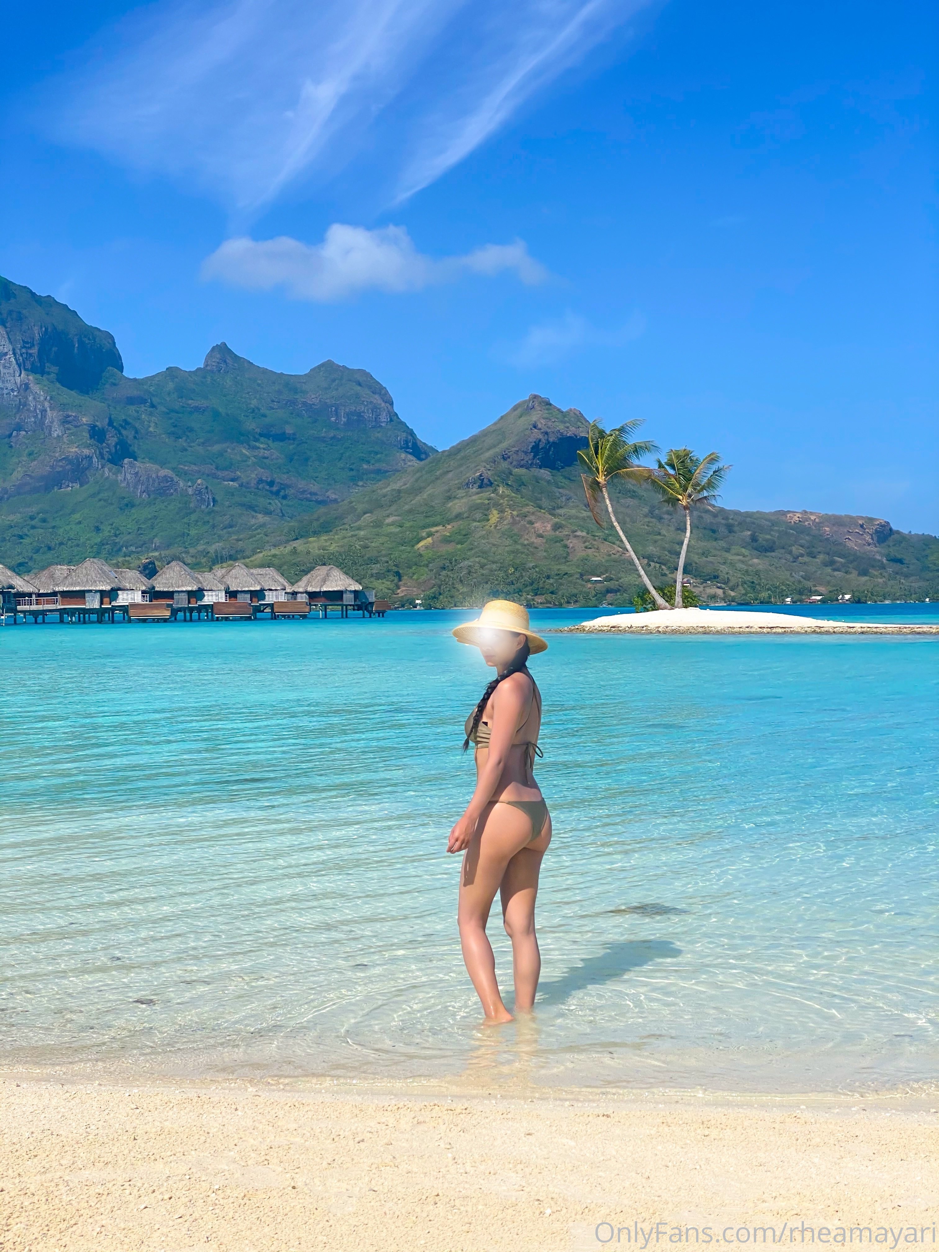 Vanessa Rallonza, a 34-year-old petite Filipino-American woman with dark brown hair, is captured in a sultry photo, showcasing her toned physique in a skimpy bikini as she walks gracefully into the ocean's embrace.